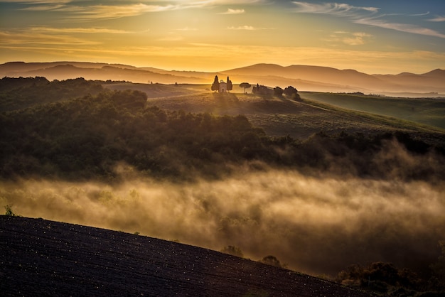 Atemberaubende Aussicht auf grüne Hügel, umgeben von Nebel mit einem Gebäude in der Ferne