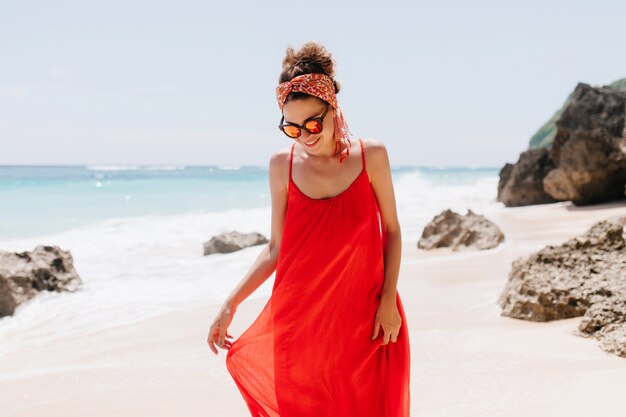 Atemberaubende kaukasische Frau, die unten schaut, während sie am wilden Strand aufwirft. Außenaufnahme der eleganten gebräunten Dame, die im Strand steht