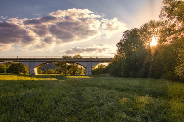 Atemberaubender Sonnenuntergang über einem grünen Wald mit einer langen Brücke in der Mitte