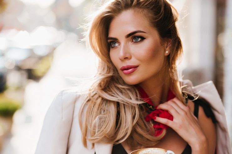 Kostenlose Foto atemberaubendes europäisches mädchen mit glamourösem make-up, das weg schaut und ihren roten schal berührt. nahaufnahmeporträt der schönen blonden frau mit den entspannenden blauen augen
