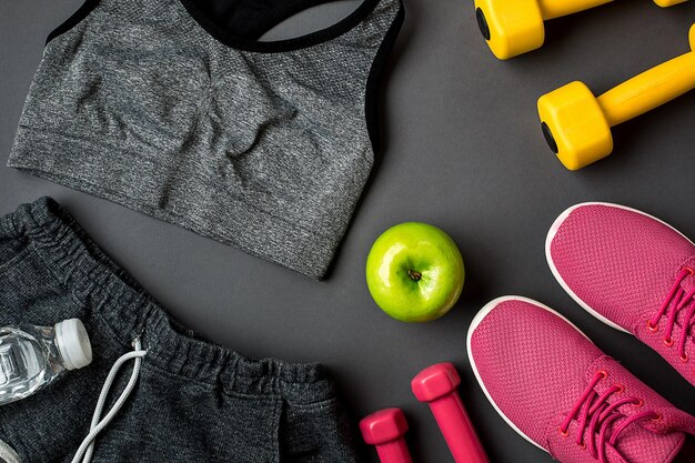 Athletenset mit weiblicher Kleidung, Turnschuhen und einer Flasche Wasser auf grauem Hintergrund