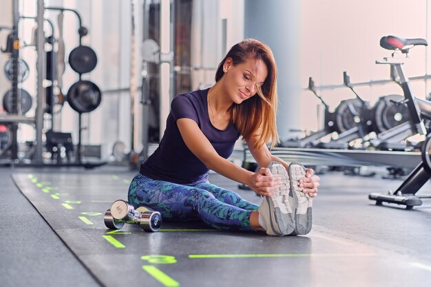 Athletische brünette Frau in farbenfroher Sportbekleidung, die sich auf einem Boden in einem Fitnessclub ausdehnt.