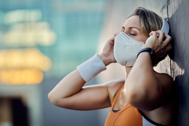 Athletische Frau mit schützender Gesichtsmaske, die Musik mit geschlossenen Augen im Freien hört