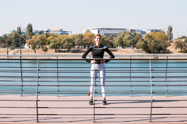 Athletische Sportlerin, die hinter dem Geländer nahe dem See steht