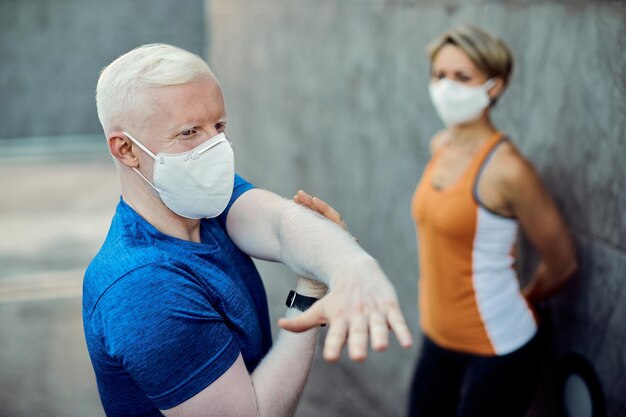 Athletischer Albino-Mann mit schützender Gesichtsmaske, der seinen Arm im Freien streckt