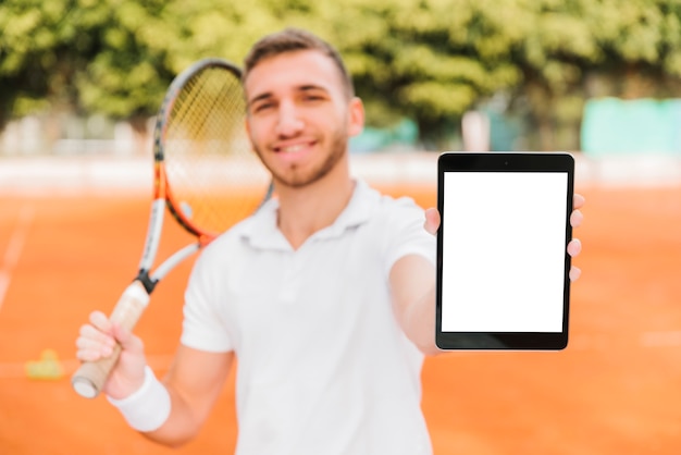 Athletischer junger Tennisspieler, der eine Tablette zeigt