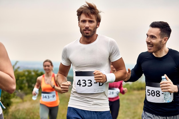 Athletischer Mann, der Marathon läuft, während sein Freund ihn während des Rennens in der Natur unterstützt