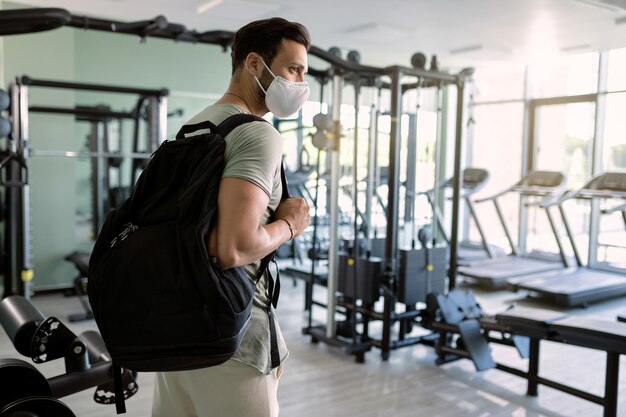 Athletischer Mann mit schützender Gesichtsmaske, der das Fitnessstudio betritt