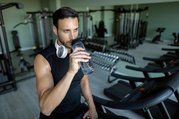 Athletischer Mann trinkt Wasser, nachdem er in einem Fitnessstudio auf dem Laufband gelaufen ist