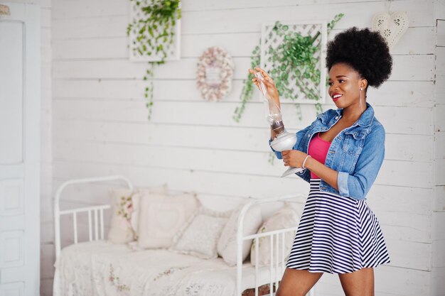 Attraktive afrikanisch-amerikanische Frau mit Afro-Haarabnutzung auf Rock und Jeansjacke posierte im weißen Raum Modisches schwarzes Modell