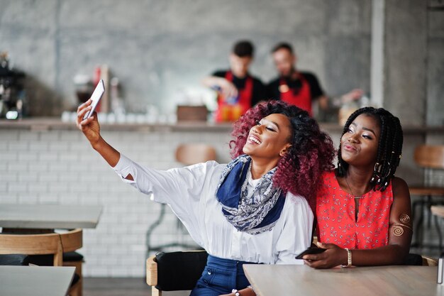 Attraktive afroamerikanische zwei Freundinnen sitzen am Tisch im Café und machen Selfie am Telefon
