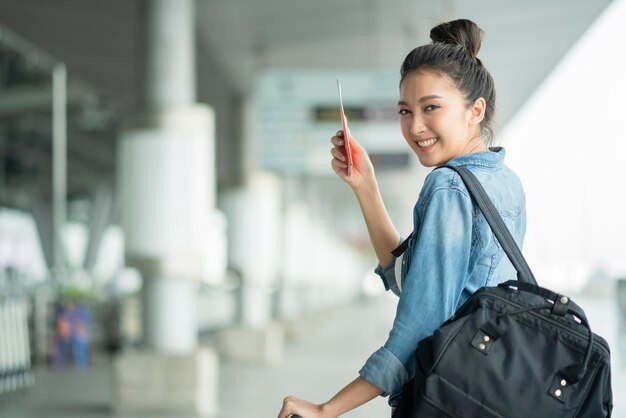 Attraktive asiatische Frau, die ein lässiges Reisetuch trägt und auf den Transitabfahrtsgebäude im Freien wartet. Reisekonzept für asiatische Frauen