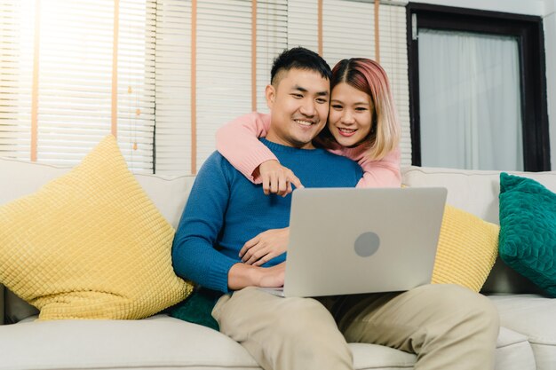 Attraktive asiatische süße Paare unter Verwendung des Computers oder des Laptops beim auf dem Sofa liegen, wenn Sie sich entspannen