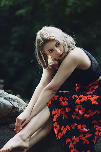 Attraktive blonde Frau mit einem Blumenkleid, das im Wald sitzt