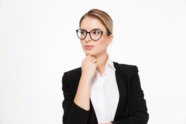 Attraktive blonde Geschäftsfrau in Brillen, die Hand nahe Kinn halten und über Weiß wegschauen
