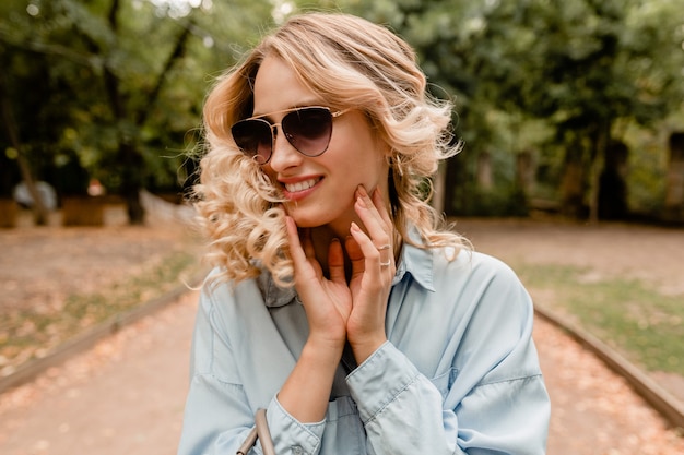 Attraktive blonde lächelnde offene Frau, die im Park im Sommeroutfit geht