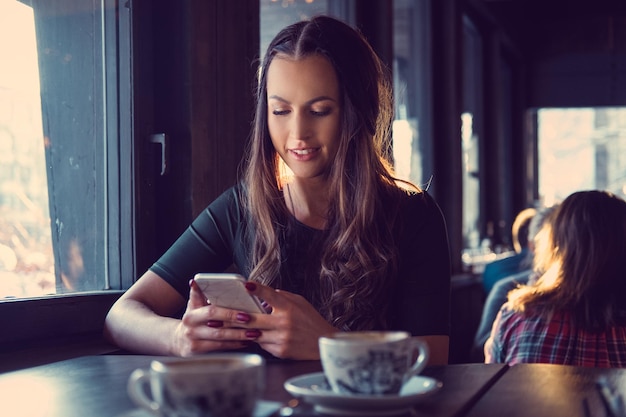 Attraktive brünette Frau, die in einem Café eine SMS schreibt.