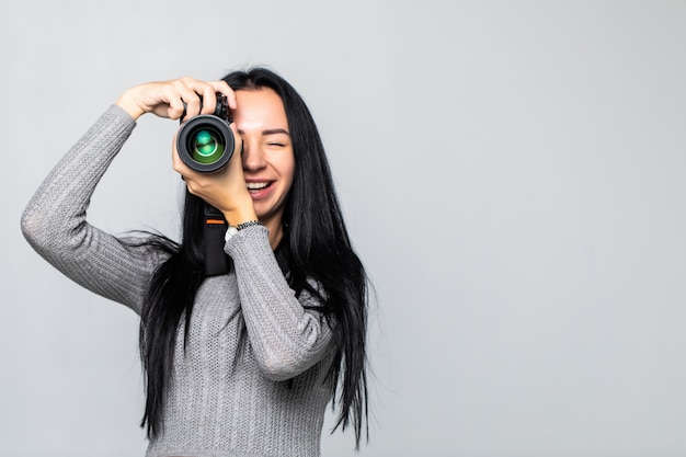 Attraktive Brünette zielt auf ihre Kamera. Komponieren eines Fotos im Studio, isoliert auf grauer Wand