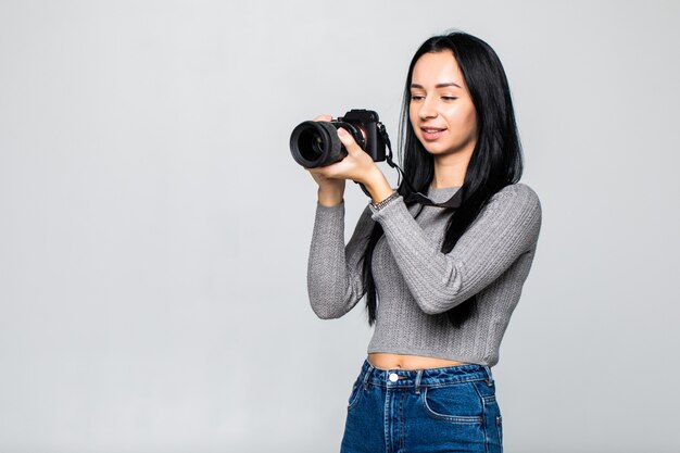 Attraktive Brünette zielt auf ihre Kamera. Komponieren eines Fotos im Studio, isoliert auf grauer Wand