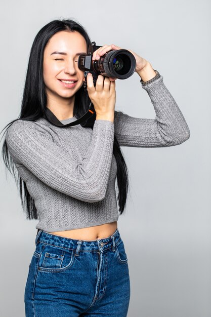 Attraktive Brünette zielt auf ihre Kamera. Komponieren eines Fotos im Studio, isoliert auf grauer Wand