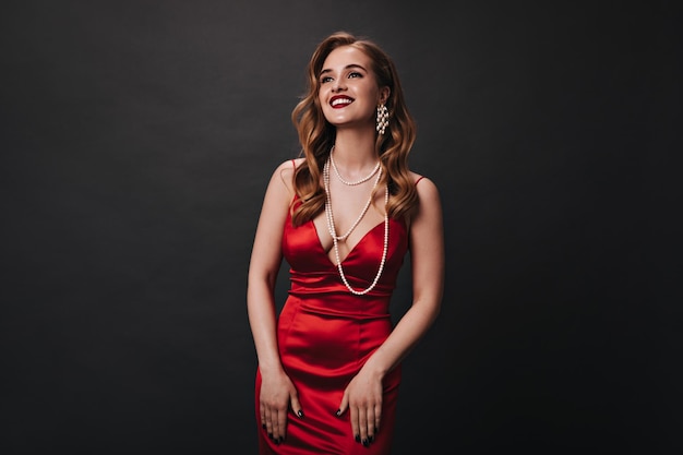 Attraktive Dame mit rotem Kleid und Schmuck mit Perlen, die auf schwarzem Hintergrund lachen