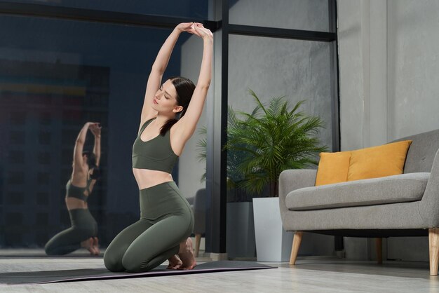 Attraktive flexible Frau sitzt barfuß auf einer Yoga-Matte und streckt sich