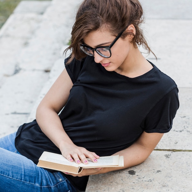 Kostenloses Foto attraktive frau, die auf treppe mit buch sich lehnt