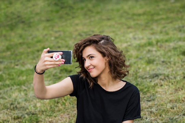 Kostenloses Foto attraktive frau, die das selfie sitzt auf rasen nimmt