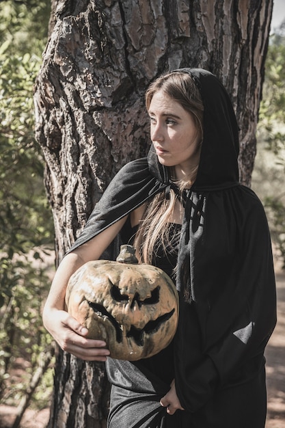 Attraktive Frau, die den Kürbis, lehnend auf Baum hält