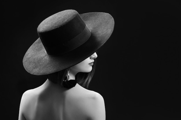 Attraktive Frau, die einen Hut trägt, der auf schwarzem Hintergrund aufwirft