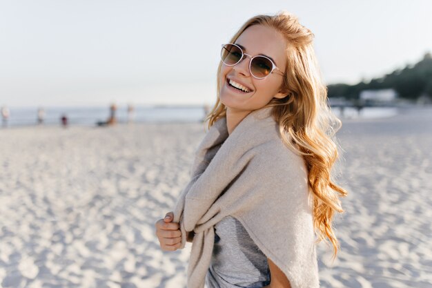 Attraktive Frau in brauner Sonnenbrille lacht am Strand