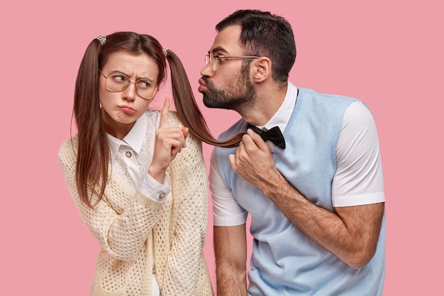 Kostenloses Foto attraktive frau mit zwei pferdeschwänzen verweigert kuss von freund, zeigt stop-geste, trägt große brille, will keine neue beziehung beginnen. schul-nerds posieren während des datums über rosa wand