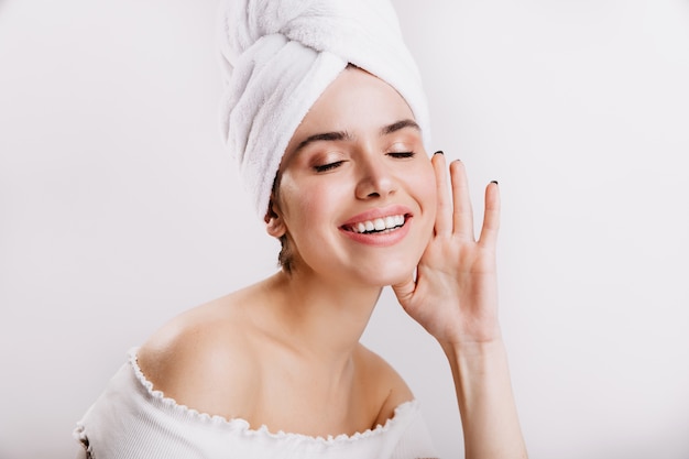 Attraktive Frau ohne Make-up posiert auf weißer Wand. Schuss von Brünette im Handtuch auf ihrem Kopf.