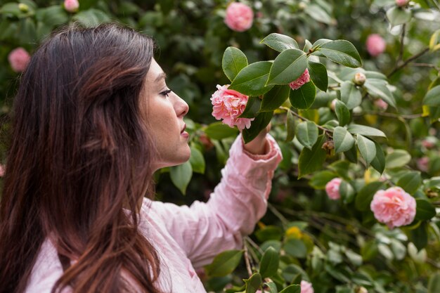 Attraktive Frau, welche die rosa Blume wächst auf grünem Zweig hält