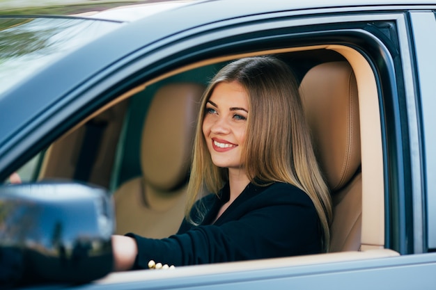 Attraktive Geschäftsfrau mit Sonnenbrille, die lächelt und ihr Auto fährt.