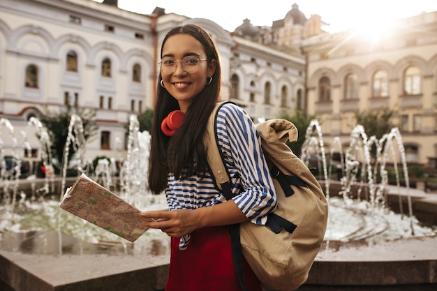 Attraktive hübsche asiatische brünette Frau ich Seidenrock, gestreiftes Hemd und Brille sieht vorne aus, lächelt