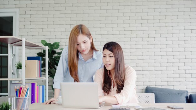Attraktive intelligente kreative asiatische Geschäftsfrauen in der intelligenten Freizeitkleidung, die an Laptop beim Sitzen arbeitet