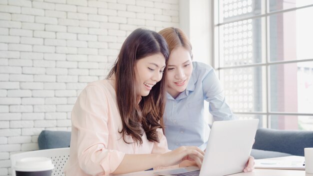 Attraktive intelligente kreative asiatische Geschäftsfrauen in der intelligenten Freizeitkleidung, die an Laptop beim Sitzen arbeitet