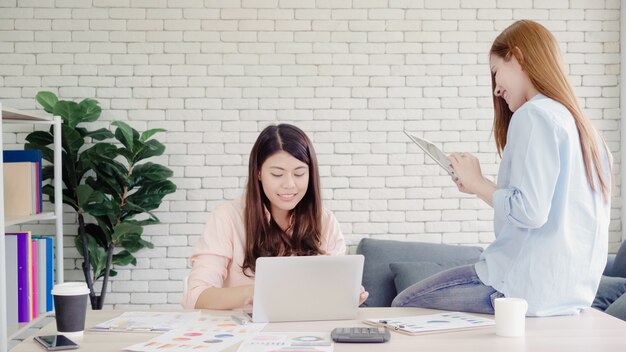 Attraktive intelligente kreative asiatische Geschäftsfrauen in der intelligenten Freizeitkleidung, die an Laptop beim Sitzen arbeitet