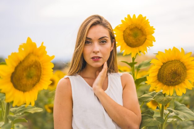 Attraktive junge blonde Frau in einem weißen Kleid posiert auf einem Sonnenblumenfeld unter dem Sonnenlicht