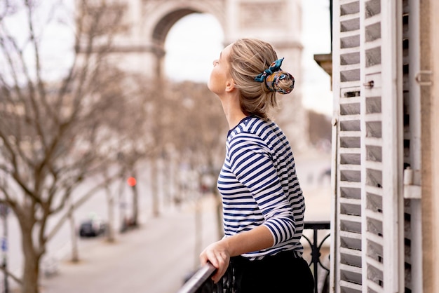 Attraktive junge Frau auf dem Balkon morgens in der Stadt Paris. Blick auf den Triumphbogen.