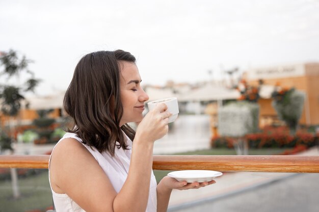 Attraktive junge Frau, die den Morgen draußen mit einer Tasse Kaffee und einer Untertasse in ihrer Hand genießt.