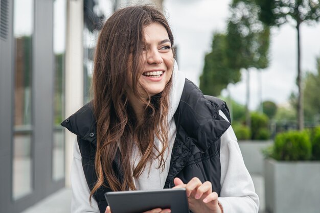 Attraktive junge Frau, die draußen ein Tablet lächelt und verwendet