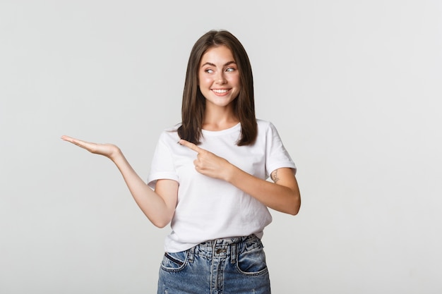 Attraktive junge Frau, die Finger auf etwas zeigt, das sie auf Hand hält.