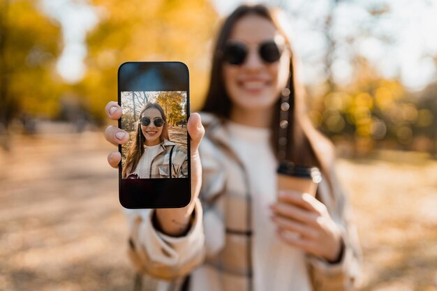 Attraktive junge Frau, die im Herbst mit Jacke mit Telefon geht