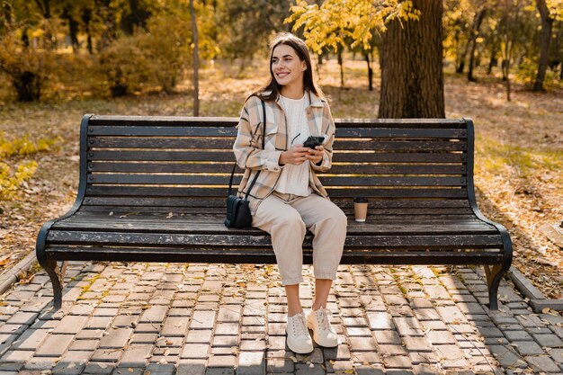 Attraktive junge Frau, die im Herbst mit Jacke mit Telefon geht