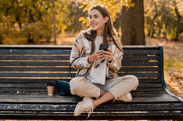 Attraktive junge Frau, die im Herbst mit Jacke mit Telefon geht