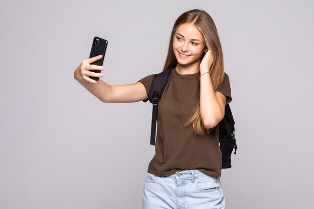 Attraktive junge Frau, die Selfies auf Handykamera auf weißer Wand macht