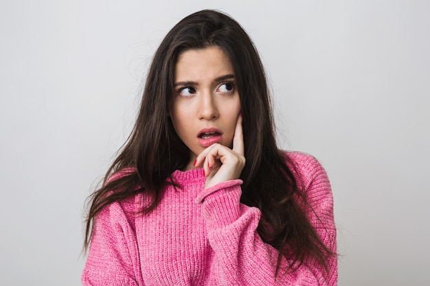 Attraktive junge Frau im rosa Pullover, überraschter Gesichtsausdruck, offener Mund, Denken, isoliert, Nahaufnahmeporträt