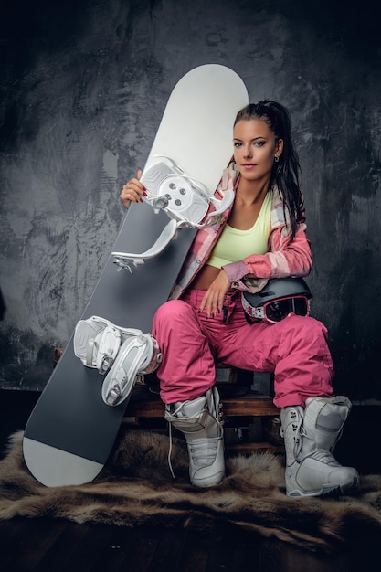 Kostenloses Foto attraktive junge frau in einem rosafarbenen snowboarderkostüm, das snowboard und schutzhelm hält.